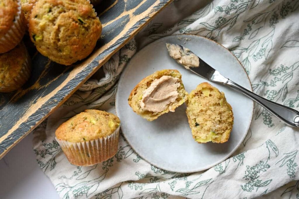 a sourdough zucchini muffin cut in half on a plate with butter