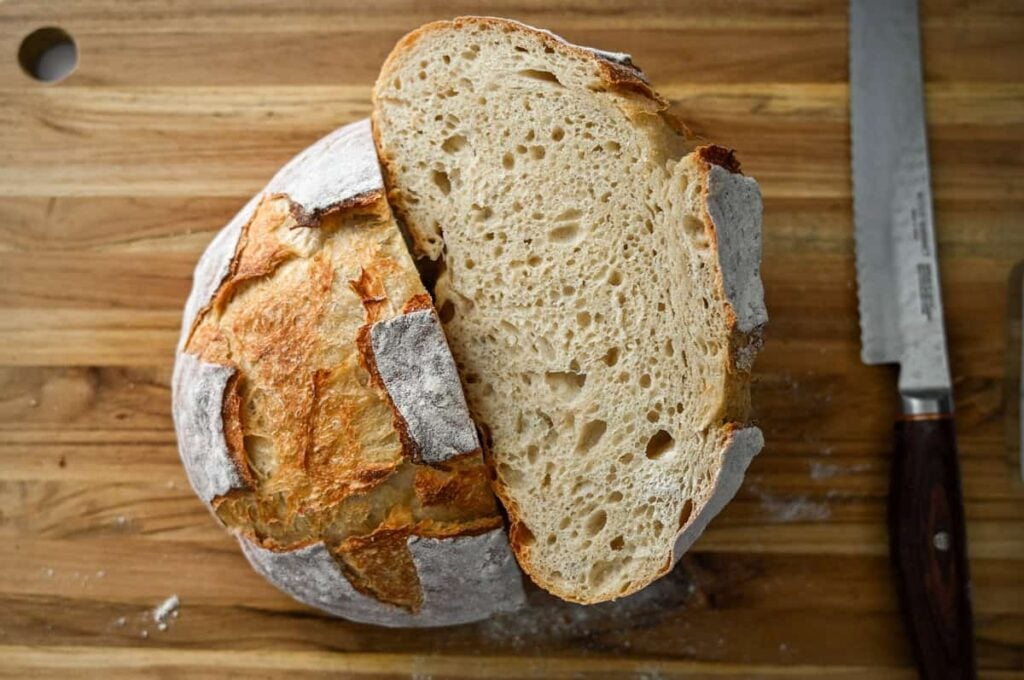 a loaf of sourdough bread cut in half on a wood cutting board