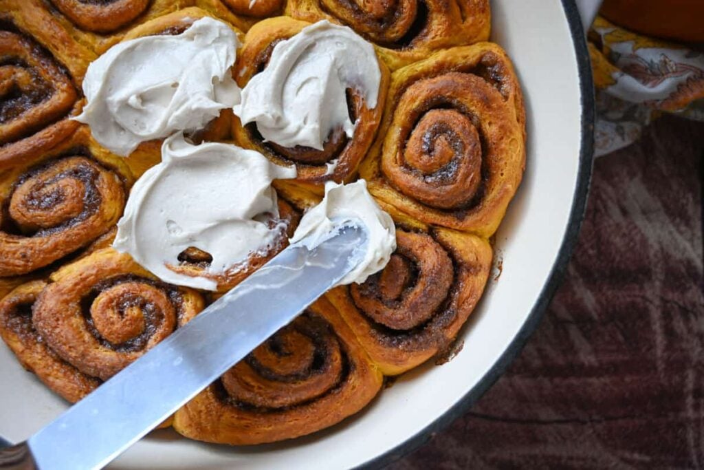 adding frosting to baked sourdough pumpkin cinnamon rolls