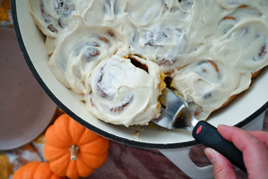 lifting a sourdough pumpkin cinnamon roll from the pan using a small spatula