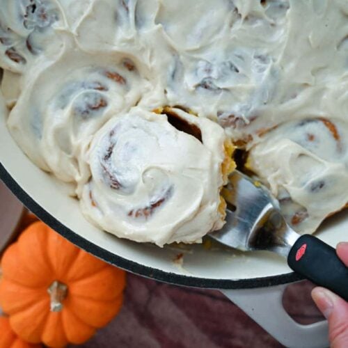 lifting a sourdough pumpkin cinnamon roll from the pan using a small spatula