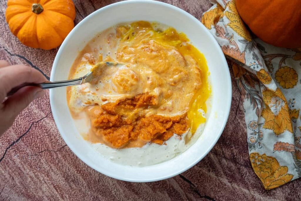 combining wet ingredients for sourdough pumpkin cinnamon rolls in a small white bowl