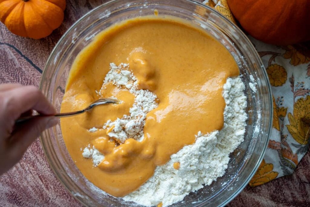combining wet and dry ingredients for sourdough pumpkin cinnamon rolls in a glass bowl